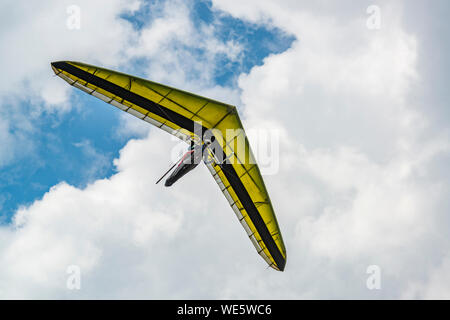 Giallo deltaplano ala con cielo nuvoloso sullo sfondo. Hangglider pilota e il suo aereo. Foto Stock