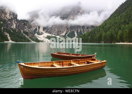 L'Italia, provincia autonoma di Bolzano, Alta Pusteria, il lago di Braies, barche sulle acque color smeraldo del lago circondato da montagne verdi catturati nella nebbia Foto Stock