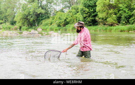 Se regolarmente del pesce si sa come gratificante e rilassante è la pesca. La pesca è un sorprendente accessibile ricreativo sport all'aperto. La pesca hobby. Barbuto brutale fisher la cattura di pesci trote con net. Foto Stock