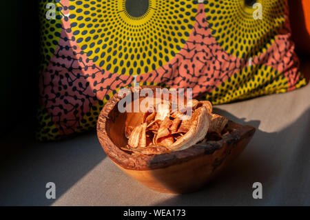 Stile Thailandese snack fritti croccanti fette di banana chip nella ciotola di legno sotto la calda luce del sole con tessuto colorato sfondo Foto Stock