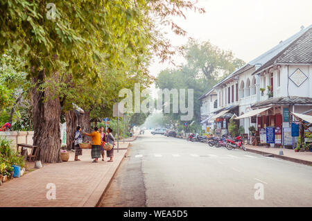 La popolazione locale al mattino street Sisavangvong Road con grande albero sul marciapiede Luang Prabang, Laos Foto Stock