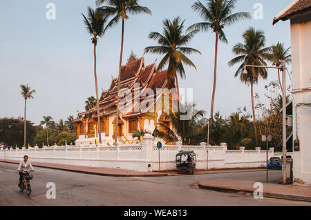 Il 4 aprile, 2019 Luang Prabang, Laos - Luang Prabang Royal Palace Museum e Hor Prabang temple hall sotto la palma da cocco con Tuk Tuk park in corrispondenza della parete laterale e Foto Stock