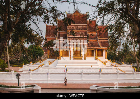 Il 4 aprile, 2019 Luang Prabang, Laos - Luang Prabang Royal Palace Museum e Hor Prabang temple hall visto throuhg rami di alberi con passeggiate lungo la strada io Foto Stock