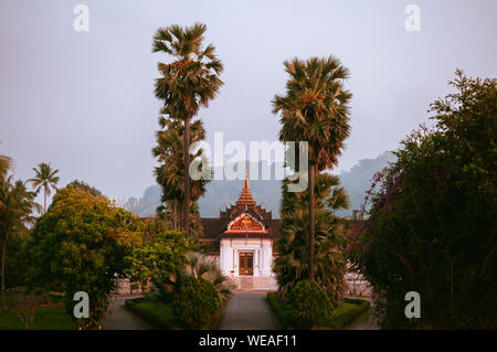 Il 4 aprile, 2019 Luang Prabang, Laos - Luang Prabang il Museo del Palazzo Reale edificio principale tra palm tree in mattinata tranquilla Foto Stock