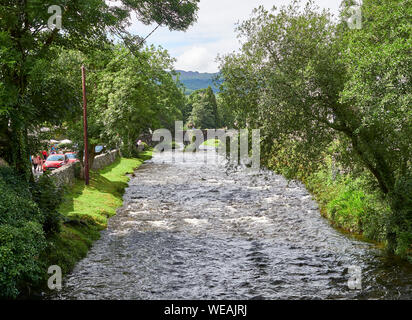 Vista del fiume Glaslyn che scorre attraverso la città di Beddgelert con alberi pieni di foglie su entrambi i lati del fiume su una giornata d'estate, Snowdonia, REGNO UNITO Foto Stock