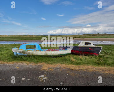 Due vecchie piccole barche da pesca insieme sat su erba accanto a un fiume con la marea sull'Isola di Anglesey, Galles del Nord, Regno Unito Foto Stock
