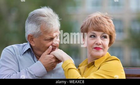 Gli amanti di età compresa tra la gente seduta su una panchina un uomo baci una donna di mano. Foto Stock