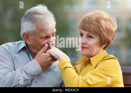 Gli amanti di età compresa tra la gente seduta su una panchina un uomo baci una donna di mano. Foto Stock