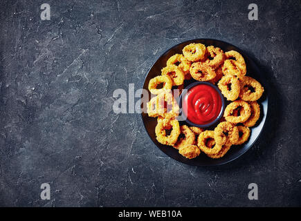 Croccanti anelli di calamari, fritte panate anelli di totano servito con salsa di pomodoro su una piastra nera su una tavola di cemento, vista orizzontale dal di sopra, libero Foto Stock