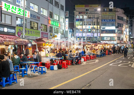 Persone seduti su sedie di plastica nella parte anteriore del cibo si spegne al mercato notturno su Donhwamun-ro 11-gil, Seoul, Corea del Sud Foto Stock