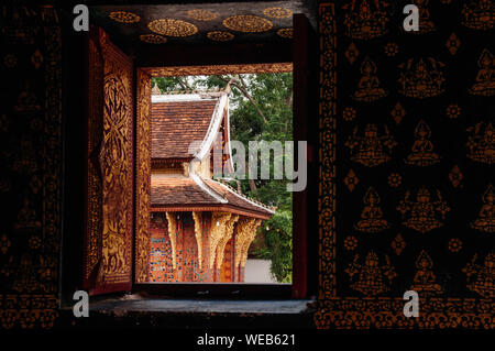 APR 5 Luang Prabang, Laos - Old Hall di Buddha visto tramite la finestra e golden buddismo arte murale di parete in corrispondenza di Wat Xieng Thong. Foto Stock