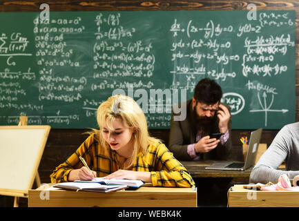 Insegnante in bicchieri leggere le relazioni di studenti di talento la correzione degli errori. Attento agli studenti di scrivere qualcosa nella loro nota pad mentre è seduto alla Foto Stock