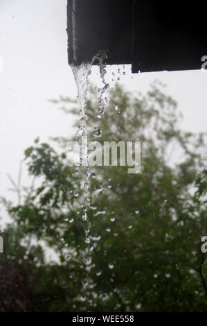 Flusso di acqua viene versata dalla grondaia. Home in pioggia intensivo. Foto Stock