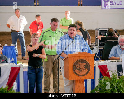 Springfield, Illinois, Stati Uniti d'America. Il 13 agosto 2019. Governatore JB Pritzker parlando al 2019 Illinois State Fair del governatore Vendita di campioni. Dipartimento di Agricoltura il regista John Sullivan in camicia verde. Foto Stock