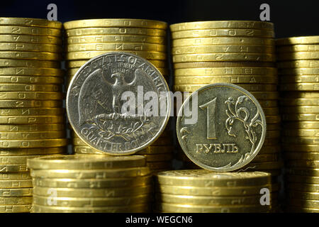 Quarto di Dollaro moneta e un rublo coin poste sui bordi di fronte a mucchi di monete Foto Stock