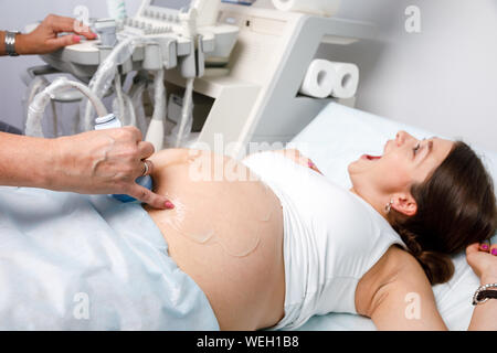 Felice giovane donna incinta con gioia guardando il suo bambino sonogram ha ricevuto una buona notizia ostetrico durante la gravidanza o procedura di ultrasuoni Foto Stock