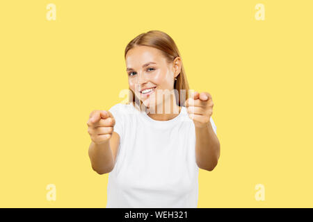 Giovani caucasici donna di mezza lunghezza verticale sul giallo di sfondo per studio. Bellissimo modello femminile in camicia bianca. Concetto di emozioni umane, l'espressione del viso. Dispositivo di puntamento su e sorridente. Foto Stock