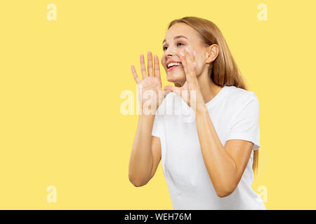 Giovani caucasici donna di mezza lunghezza verticale sul giallo di sfondo per studio. Bellissimo modello femminile in camicia bianca. Concetto di emozioni umane, espressione facciale, vendite. Saluto, chiamando qualcuno. Foto Stock