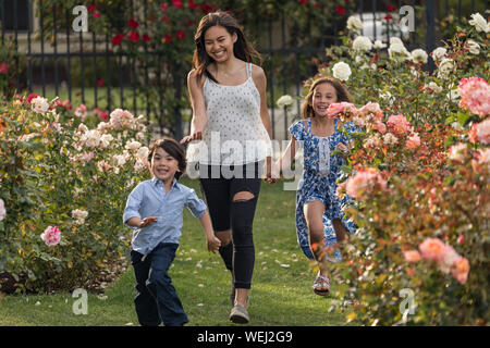 Sorelle e fratelli dell Asia e dell etnia miste in esecuzione e ridere insieme nel giardino di rose, San Jose, California Foto Stock