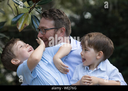 Padre con 4 e 2 anno vecchio figli seduti sulla panchina nel parco parlando Foto Stock