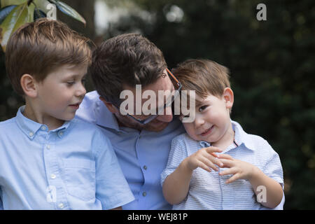Padre con 4 e 2 anno vecchio figli seduti sulla panchina nel parco parlando Foto Stock