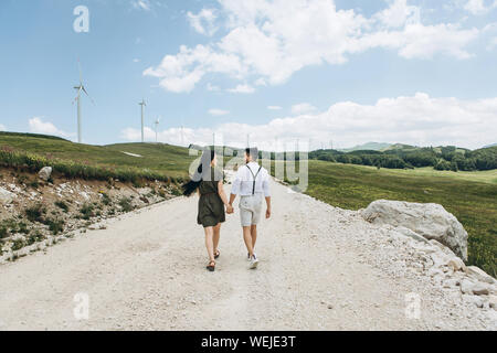 Una giovane coppia tiene per mano e camminare insieme lungo la strada. Foto Stock
