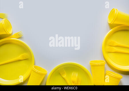 Uso singola giallo picnic utensili, piatti, tazze, forche su grigio. Ambiente, eco friendly, immondizia di plastica per riciclare il concetto. Vista dall'alto. Spazio per te Foto Stock