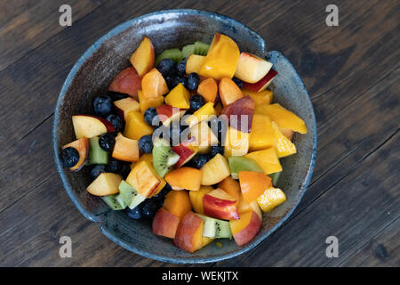 Multicolore fresca insalata di frutta in blu e nero fatto a mano ciotola sul tavolo al giorno, sfondo sfocato, angolo alto Foto Stock