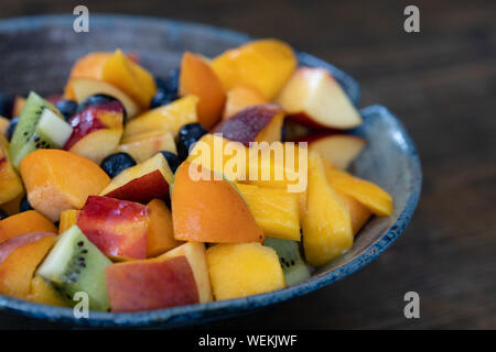 Multicolore fresca insalata di frutta in blu e nero fatto a mano ciotola sul tavolo al giorno, sfondo sfocato, close up Foto Stock