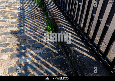 Pali recinzione con lunghe ombre su un percorso di pietra Foto Stock