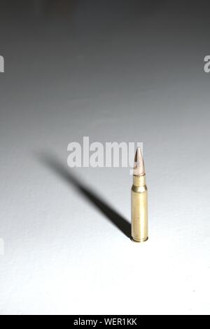 Un grande bullet (7,62 x 51 mm) nato in piedi su una superficie bianca con lunghi drammatico. Lo sfondo è un gradiente di colore nero. Foto Stock