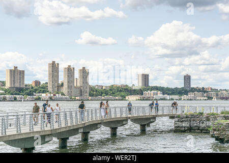 Wpeople affollano un ponte pedonale attraverso piccole ingresso nel fiume Hudson River Park con ampia vista di acqua e varietà bassa & highrise alloggiamento sul New Jersey Shore Foto Stock