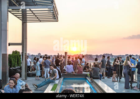 La pace come giovane folla si raduna in sala stampa New York bar sul tetto terrazza per socializzare e sentirsi momento magico quando il sole scivola al di sotto del New Jersey skyline Foto Stock