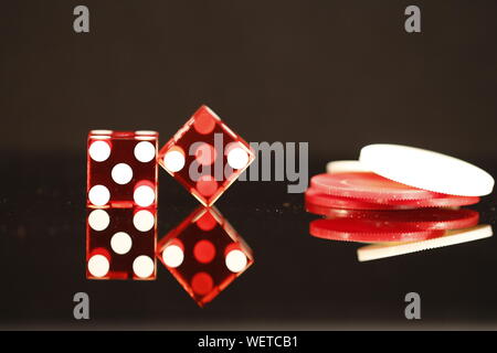 Due dadi rossi pari a 7 con il rosso e bianco poker chips su un nero sfondo riflettente Foto Stock