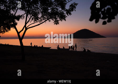 Il lago Malawi a Monkey Bay, gente radunarsi compresi in teh Beach, lavaggio piatti, parlando, rosso tramonto, sud-est-africa Foto Stock