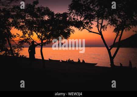 Il lago Malawi a Monkey Bay, gente radunarsi compresi in teh Beach, lavaggio piatti, parlando, rosso tramonto, sud-est-africa Foto Stock