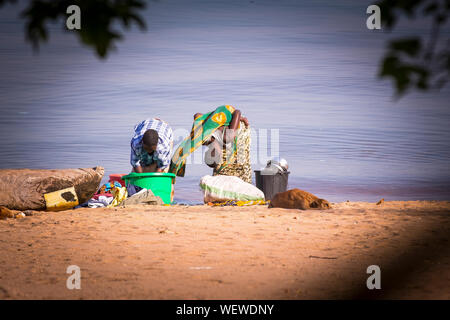 Il lago Malawi, Monkey Bay, donna portare il suo bambino, lavare i vestiti in spiaggia, sud-est-africa Foto Stock