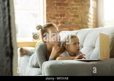 Femmina insegnante caucasica e bambina, o la mamma e figlia. Homeschooling. Sdraiato sul divano e utilizzando il laptop per ottenere conoscenze durante la lezione è. Istruzione, scuola, studiando concetto. Foto Stock