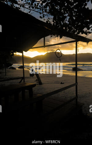Vista di un tramonto mozzafiato attraverso le montagne e dalla spiaggia con la luce del sole che riflette in mare Foto Stock