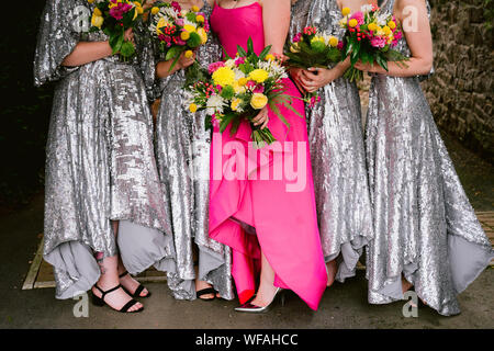 sposa in abito rosa con bridesmaids in abiti in paillettes argento, tutti con bouquet luminosi Foto Stock