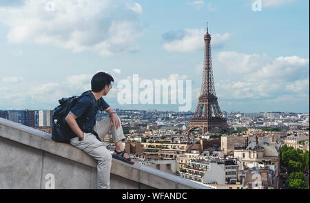 Un uomo con zaino guardando la torre Eiffel, famoso punto di riferimento e meta di viaggio a Parigi, Francia Foto Stock