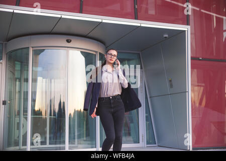 Occupato donna telefona al momento di lasciare l'edificio degli uffici. Foto Stock