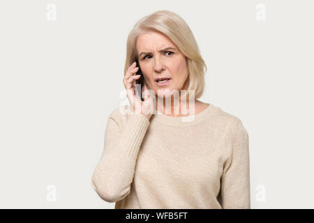 Signora matura isolata su sfondo grigio utilizza lo smartphone a parlare Foto Stock