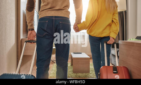 Ritagliato Ritratto di giovane donna e uomo in abbigliamento casual con le valigie di entrare nella loro camera di un hotel. Essi detengono reciprocamente le mani. Viaggiano insieme il concetto. Inquadratura orizzontale. Vista posteriore Foto Stock