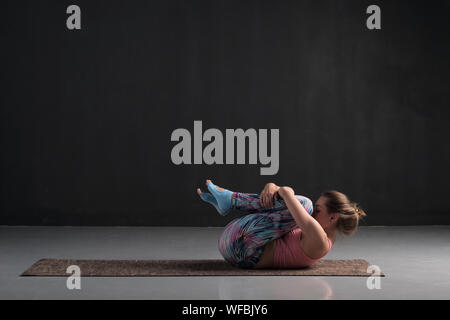 Giovani caucasici ragazza Apanasana facendo yoga posa per lo stomaco sano e relax dopo una dura pratica. Foto Stock