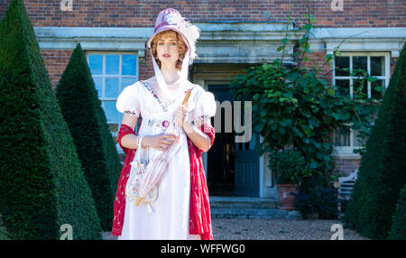 Bella donna che indossa vintage abito regency e cofano, portando un ombrellone e di stare al di fuori della sede statali Foto Stock