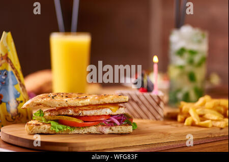 Il fast food servita tabella per la compagnia di amici. hamburger, patatine fritte e bevande al compleanno servita tabella. bambini compleanno composizione alimentare con torta con Foto Stock