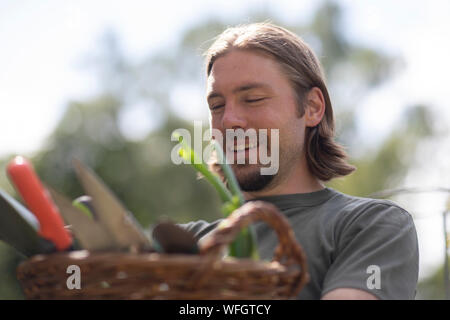 Ritratto di un uomo che porta un cesto pieno di attrezzature da giardinaggio, Germania Foto Stock