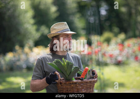 Ritratto di un uomo in piedi in un giardino che porta un cesto pieno di attrezzature da giardinaggio, Germania Foto Stock