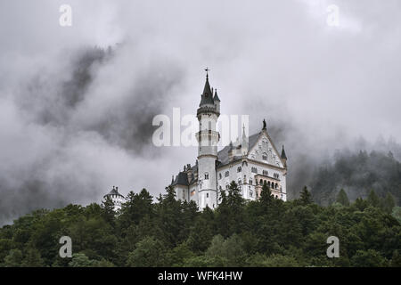 Il Castello di Neuschwanstein (Schloss Neuschwanstein) dalla città di seguito, circondato dalla nebbia e alberi - a Schwangau, Germania Foto Stock